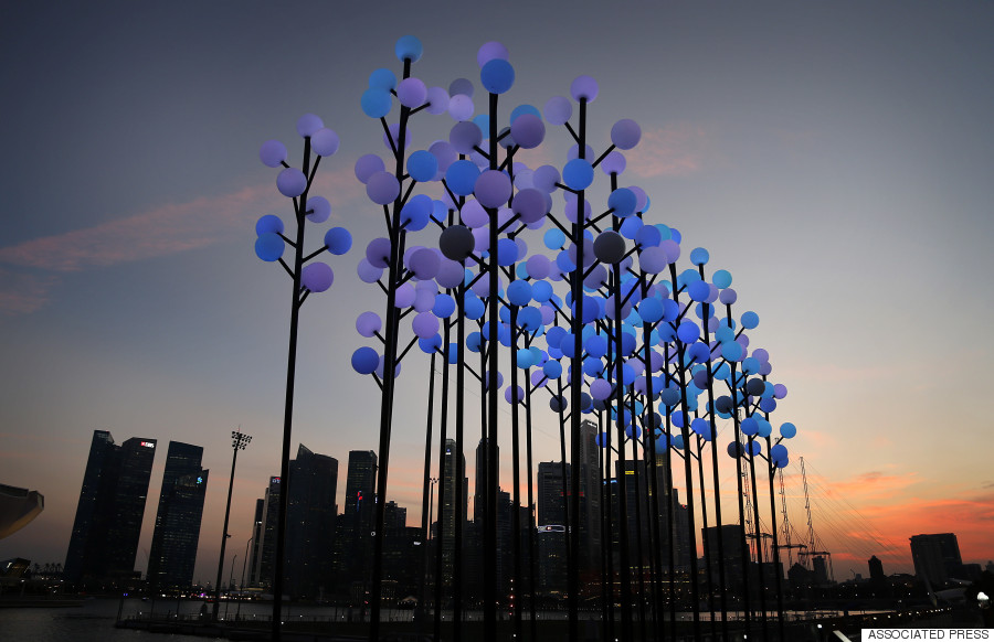 A photograph of a city skyline at dusk with lamps in the foreground that resemble stylized trees.