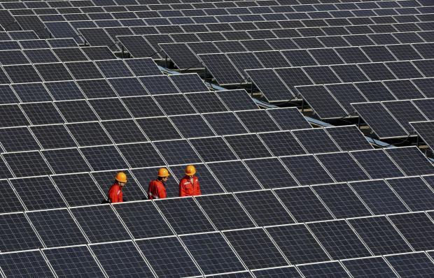Workers walk among newly installed solar panels at a solar power plant in Zhouquan township of Tongxiang, Zhejiang province December 18, 2014. A new report highlights the co-benefits of renewable energy sector. REUTERS/Stringer 